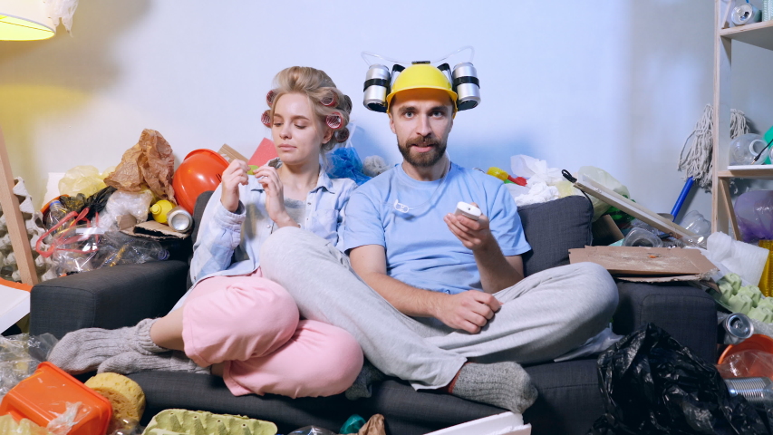 Man and woman sitting together on the sofa and watching tv. Manl looks like fotball fan, emotioanal and happy. Woman is no emotioanal and egnoring him.