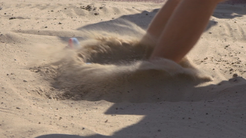 Sportsman doing long jump landing in sandpit. Track and field championships. Athlete competing in long jump. Volleyball game in the sand. Beach football.