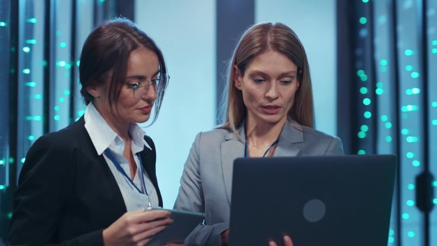 Professional female engineers in IT data center networking on notebook running deep diagnostics of database server cabinet. Two women working in team at cyber security.