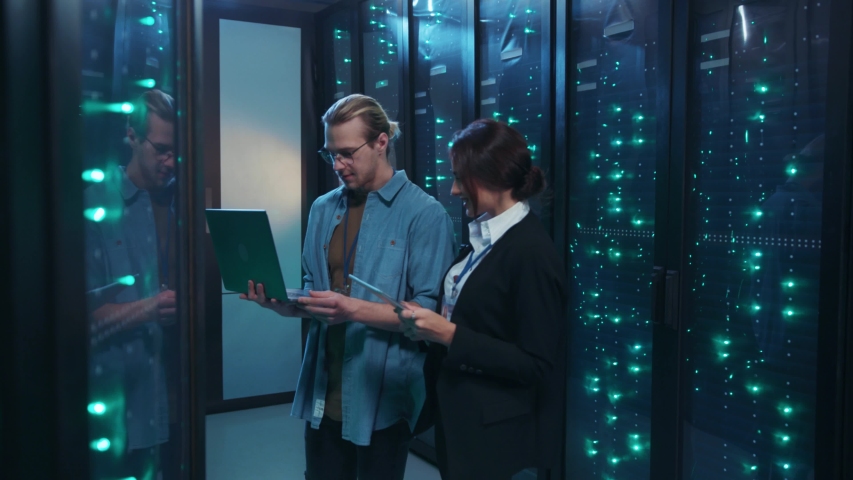 IT technician with female engineer starting a dance moving with laptop inside server rack corridor having fun together. Comical team of data center. Concept of humor.