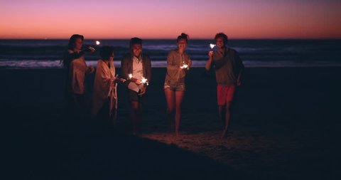 Friends on the beach holding sparklers celebrating at sunset RED DRAGON