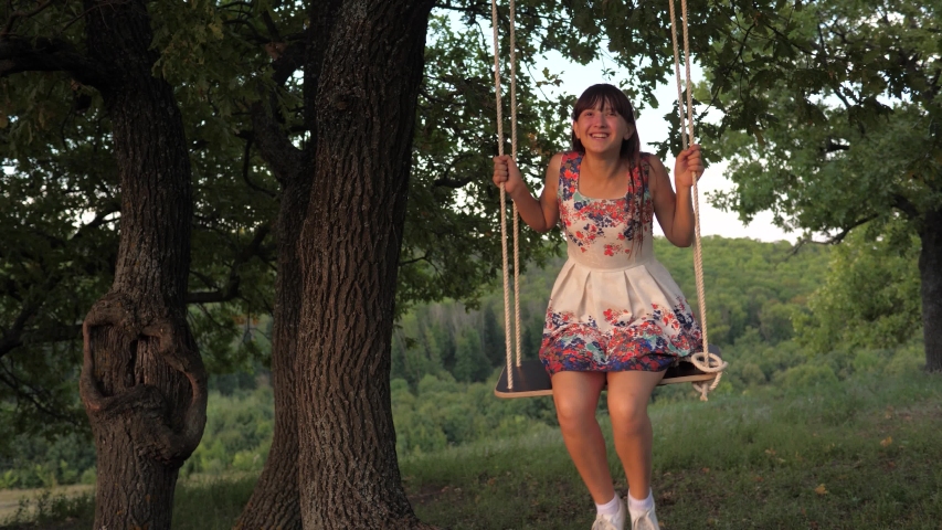 child swinging on a swing in park in sun. teen girl enjoys flight on swing on summer evening in forest. concept of happy family and childhood.