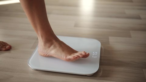 Girl Legs Step On Bathroom Scale. Woman On Scales Measure Weight. Human Barefoot Measuring Body Fat Overweight. Slim Woman Checking BMI Weight Loss. Diet Female Feet Standing Weighing Scales On Room