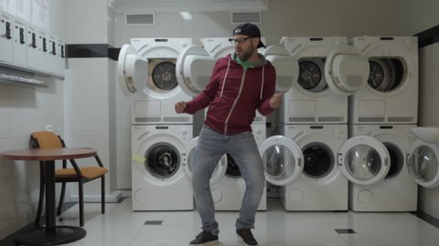 Man Dancing Viral Dance And Have Fun In the Laundry Room. Happy Guy Enjoying Dance, Having Fun Together, Party. Joyful Man With beard in Cap and Glasses Dancing Cheerful In Laundry Room. Slow Motion.
