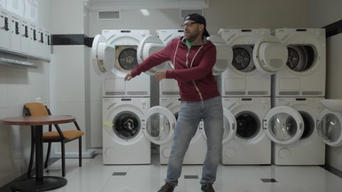Man Dancing Viral Dance And Have Fun In the Laundry Room. Happy Guy Enjoying Dance, Having Fun Together, Party. Joyful Man With beard in Cap and Glasses Dancing Cheerful In Laundry Room. Slow Motion.
