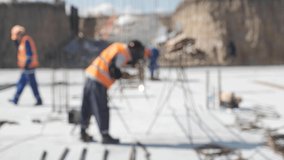 Builders in overalls and protective helmets perform work on the construction site. The work of an electric welder. Working activity. The video is out of focus for use as a background image.