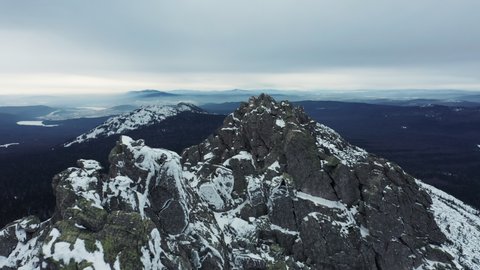 Winter day in Taganay national park; mountain ridge Otkliknoy greben' with steep snowy slopes and rocky peaks; deep taiga forest at the foot of mount; panorama of foggy mountain terrain in background