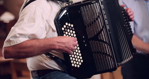 Close up slow motion shot, musician  playing accordion inside small inn, cottage, double bass in background, 4K.