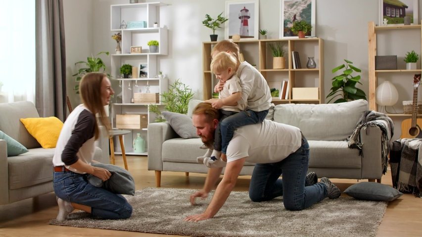 Young dad crawling on floor carrying cute small child sons on back