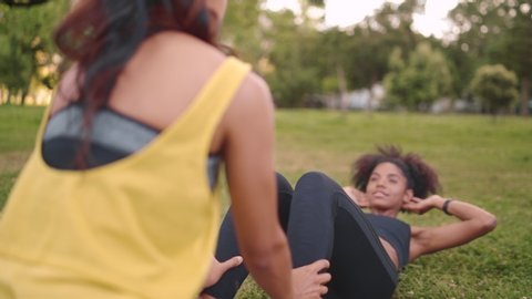 Young woman doing sit-ups with assistance of her female friend in the park - friends doing exercise in the park supporting eachother Stockvideó