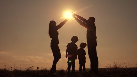 happy family teamwork silhouette shows a house and comfort symbol at sunset. mom dad and kids children portray a house roof hold their hands over their heads lifestyle
