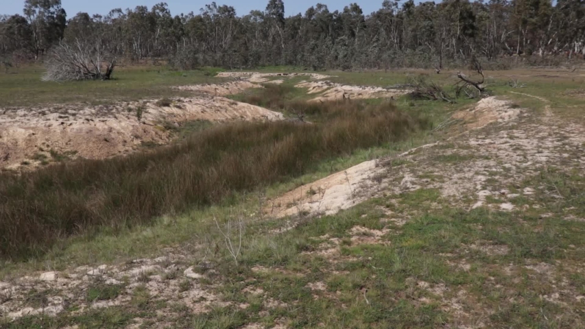 Empty stream bed in a dried up lake, Australian bush in the distance, right to left pan.