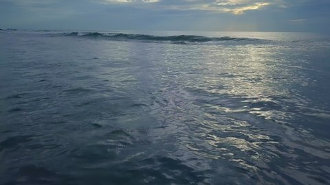 The dawn of the morning dawns on the sea. The waves in the middle of the sea roll slowly, and the waves are beating against the beach, showing a detailed appearance.