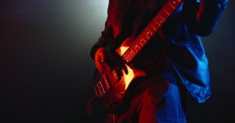 A cool guitar music performer starring on stage. Authentic grunge musician making a solo on bass guitar lit by red and blue neon lights 4k footage