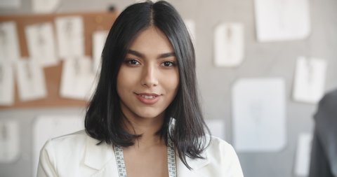 Close-up portrait of successful female clothes designer at her office, looking at camera and smiling - fashion concept 4k footage