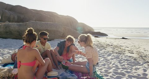 Multi ethnic Group of friends on the beach hanging out eating watermelon RED DRAGON