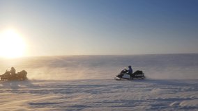 People go on snowmobiles in the Arctic. Snowmobiles with trailers, which is different equipment. The setting Sun is on the horizon. Video made in Russia. The Taimyr Peninsula.