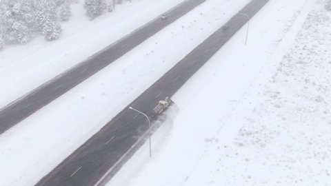 DRONE: Flying above a wintry evergreen forest as snowplow clears the icy highway in Washington, USA. Truck ploughs fresh snow gathered on the side of an asphalt freeway. Truck cleaning the icy road.