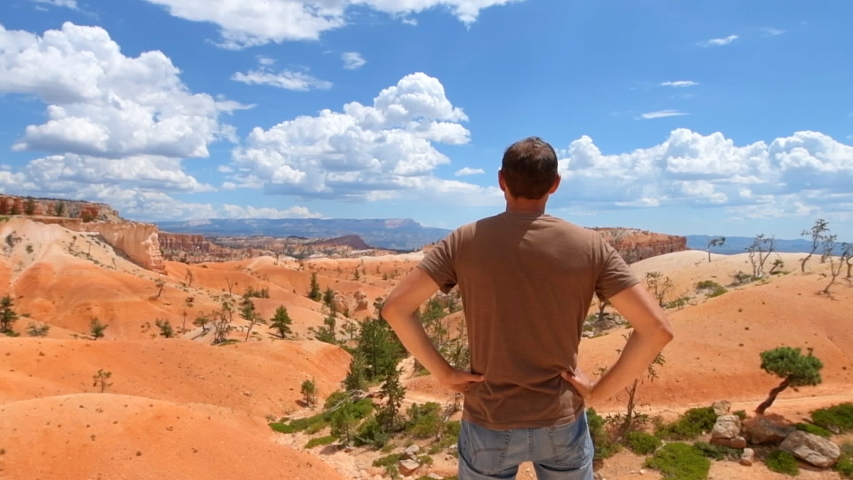Man tourist person turning around in slow motion by orange color formations at Queens Garden Navajo Loop trail at Bryce Canyon National Park in Utah happy