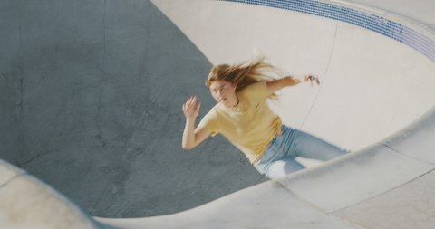 Girls in extreme sports, stylish retro skater girl does a surf style carving turn on her skateboard in a concrete skate pool bowl