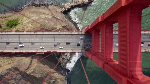 Many vehicles drive along the Golden Gate Bridge road. Bridge roadbed goes from above the water and to the land. Aerial topdown footage. Famous tourist attraction of San Francisco, California. 4k