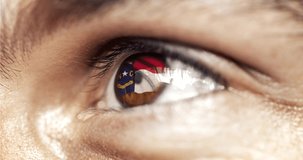 man brown eye in close up with the flag of North Carolina state in iris, united states of america with wind motion. video concept