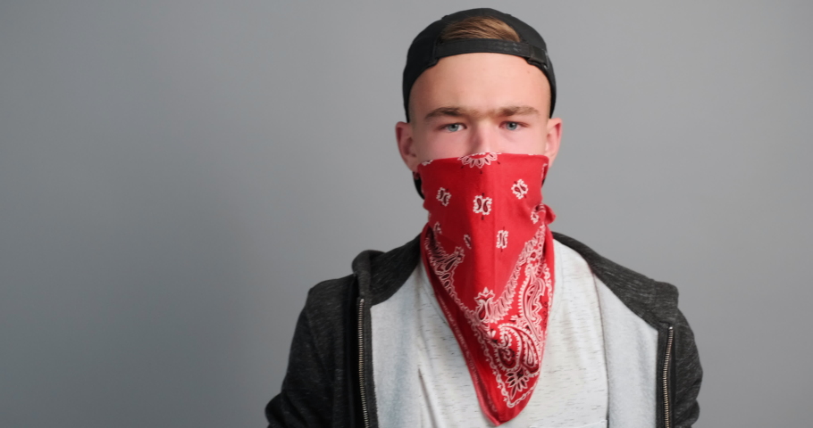 Portrait of young angry protester teenager boy hides his face behind flag USA and punches camera on a grey background. Football fan. Aggression. Protests. Independence. Freedom, rebels. Copy space