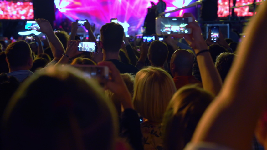 Ukraine, Kyiv, July 19, 2019: Free concert. Happy people are watching an amazing musical concert. Merry fans jump and raise their hands up. Fans are filming a concert on a smartphone. Live concert. | Shutterstock HD Video #1042305352