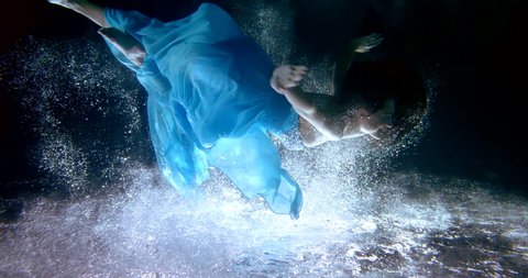 A young slender girl in a dress falls into the water. Underwater art shooting in the pool. Immersion in another reality
