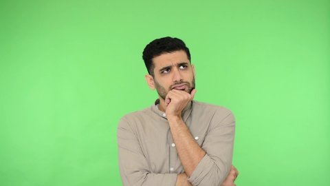 Smart thoughtful brunette man in shirt holding his chin and seriously considering problem solution, looking confused doubtful while making difficult choice. studio shot, green background, chroma key