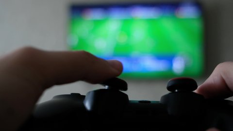 Close view of a gamer's hands playing soccer (football, fifa) simulator video game on console using joystick.