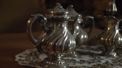 A close up slow panning on a vintage silverware teapot, milk pan and sugar bowl near ancient decorative venetian carnival mask 