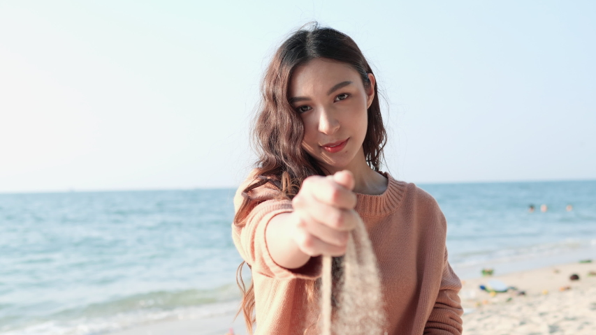 Asian beautiful teenage girl happy and smiling at seaside beach summer. Woman grabs a handful of dry sand and lets it fall. | Shutterstock HD Video #1042323265