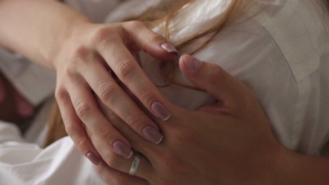 Close-up of the hand of a man hugging his girlfriend by the shoulders on the bed in the bedroom. A man gently stroking his girlfriend's hand, close-up. Slow motion.