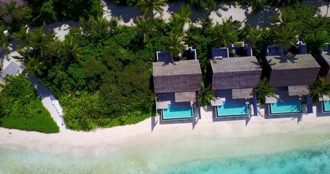 overwater bungalow houses on the white sand beach, clear blue-green water and white sand beach, palm trees surrounding the hotel