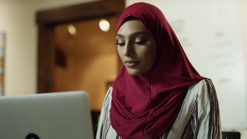 Close up of woman wearing hijab using laptop then closing lid and leaving / Cedar Hills, Utah, United States