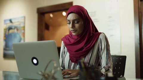 Close up of serious woman wearing hijab typing on laptop / Cedar Hills, Utah, United States