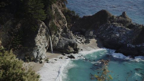 High angle view of waves splashing on rocks in ocean near waterfall / Big Sur, California, United States
