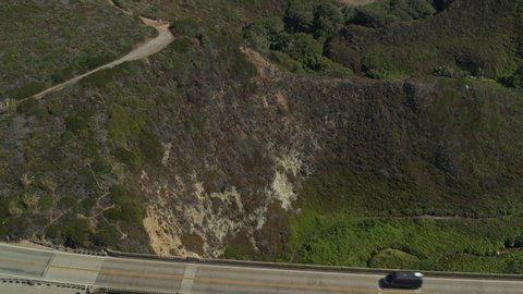 Aerial view of cars driving on bridge at rocky coast near ocean waves / Big Sur, California, United States