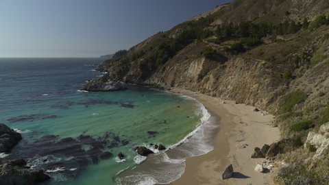 Aerial view zooming out from ocean waves on beach / Big Sur, California, United States