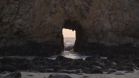 Ocean waves splashing though Keyhole Arch at sunset / Big Sur, California, United States