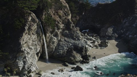 High angle view of waves splashing on rocks in ocean near waterfall / Big Sur, California, United States