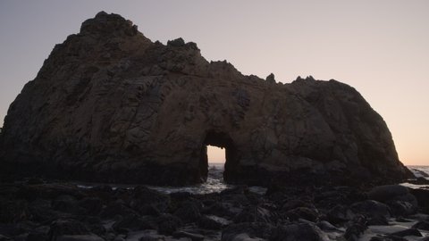 Ocean waves splashing though Keyhole Arch at sunset / Big Sur, California, United States