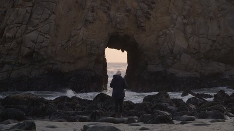 Woman photographing Keyhole Arch at sunset / Big Sur, California, United States