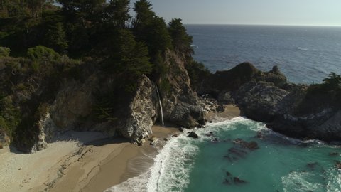 Aerial view of waves splashing on rocks in ocean near waterfall / Big Sur, California, United States