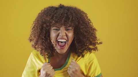 Brazilian supporter. Brazilian woman fan celebrating on soccer, footbal match on yellow background. Brazil colors. Cheering woman in a Brazilian shirt. 4K.