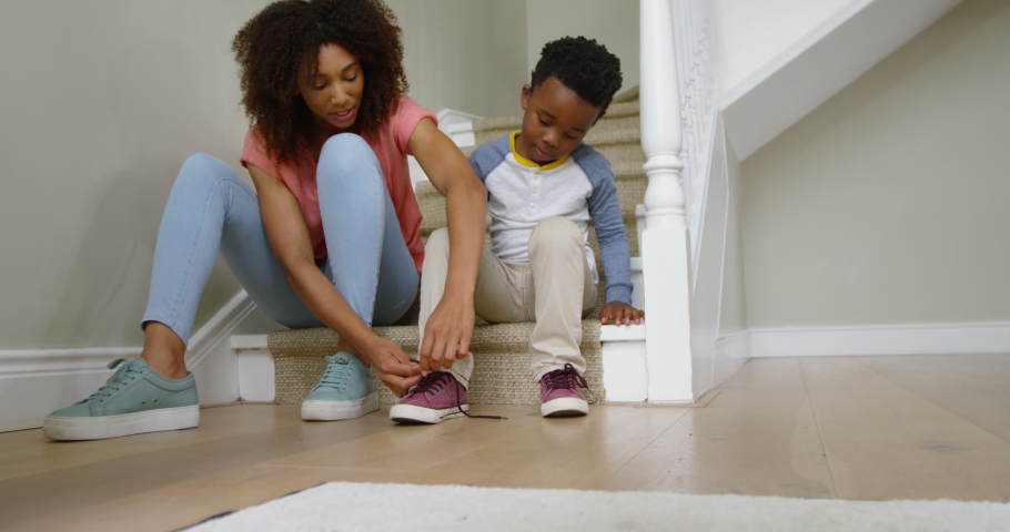 Front view of an african american mother and her young son sitting on the stairs in the hallway at home. Social distancing and self isolation in quarantine lockdown for Coronavirus Covid19 | Shutterstock HD Video #1042345066