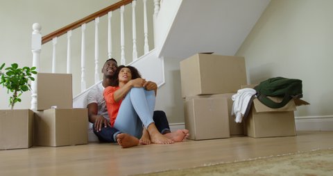 African American couple sitting on the floor together in front of a pile of boxes in the hallway of their new home. Social distancing and self isolation in quarantine lockdown for Coronavirus Covid19