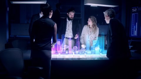 Businessman in suit talking to business people Colleagues or Partners standing around Futuristic table with light showing an Architecture Project powered by a Holographic modern Projection Software.