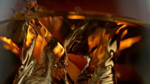 Super Slow Motion Detail Shot of Ice Drop into Glass with Whiskey at 1000fps.